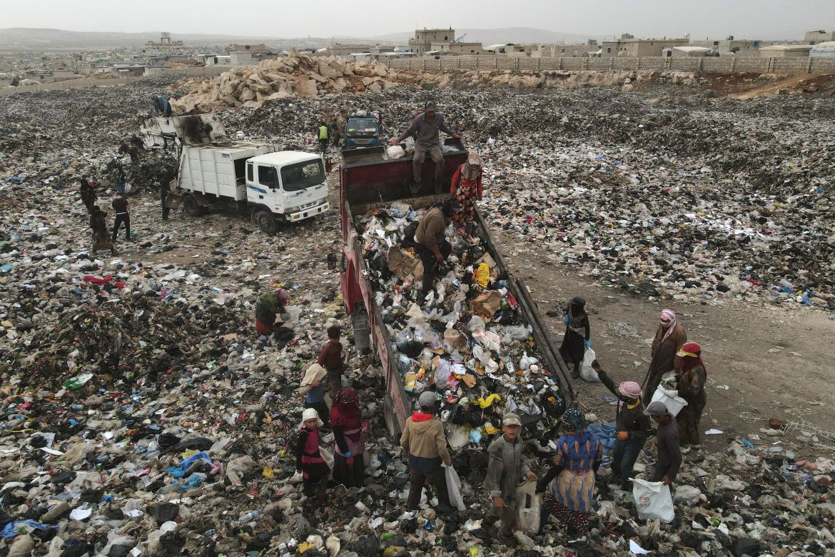 In this picture taken on June 3, 2023, people surround rubbish trucks as they unload at a dump site, to collect plastic items to sell for recycling, near the village of Hazreh in Syria's northwestern Idlib province.