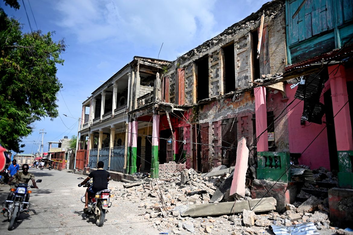 People drive past damaged buildings in Jeremie, Haiti,