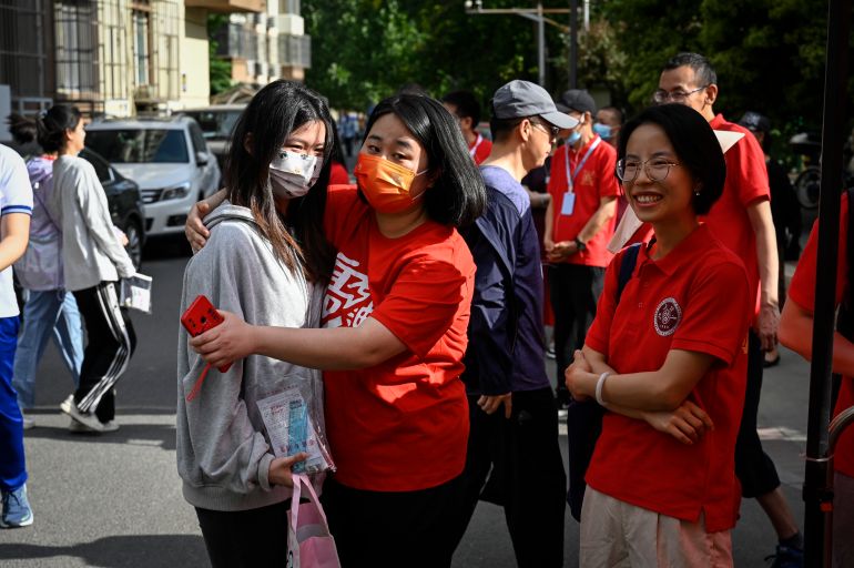A teacher hugs a student on the first day of the gaokao. There are parents around. They are wearing red for luck.