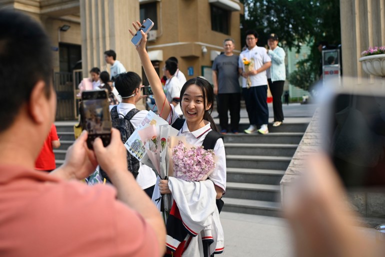 A student holding a bouquet of flowers after finishing the Gao Kao.  She is holding her right arm up and smiling.  She looks very happy.