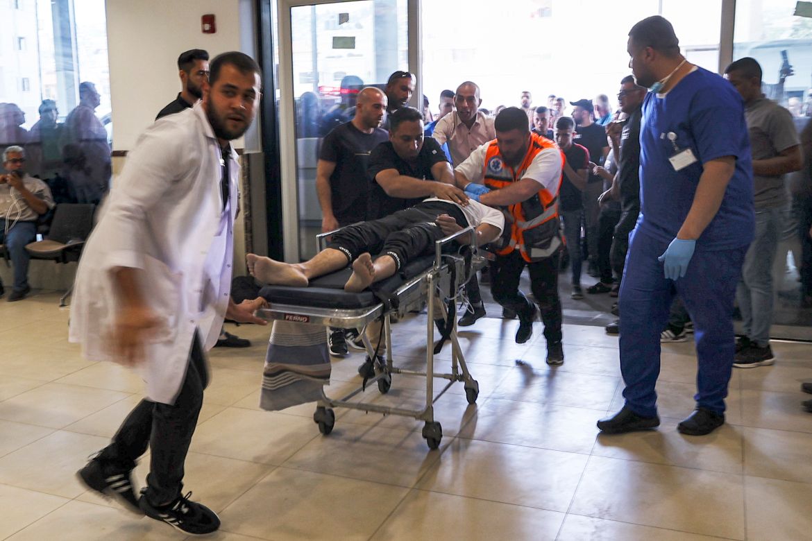 An injured man lying on a gurney is rushed by paramedics upon arrival at a hospital in Jenin