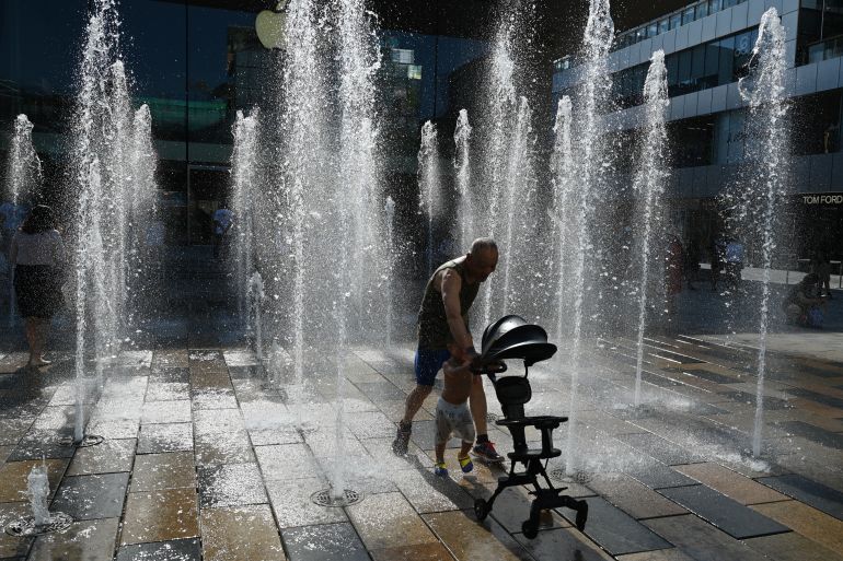 A man playing with his young child in fountains in Beijing. It looks hot.