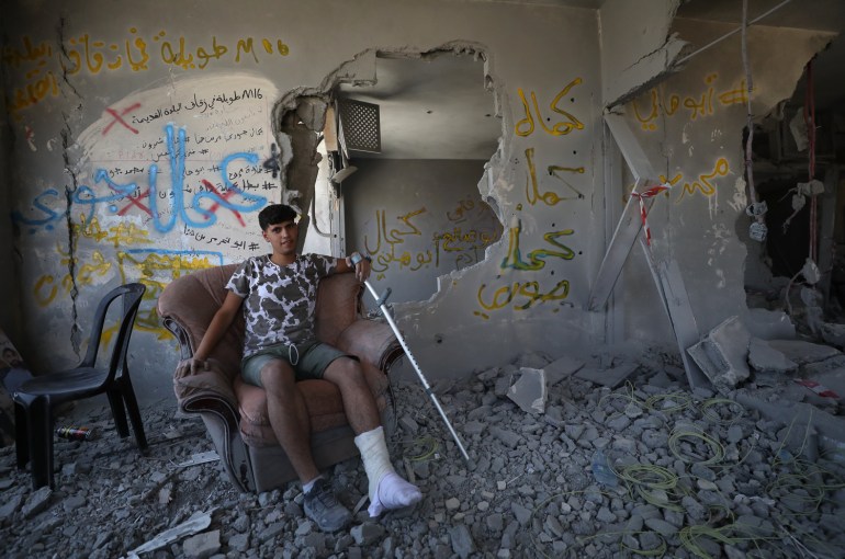 usaid on a broken armchair with his leg in a cast in the destroyed home