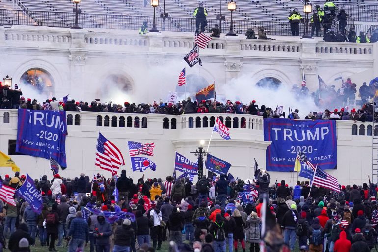 Rioters gather with Trump signs before the steps of the US Capitol. Smoke or tear gas can be seen rising from the crowd.