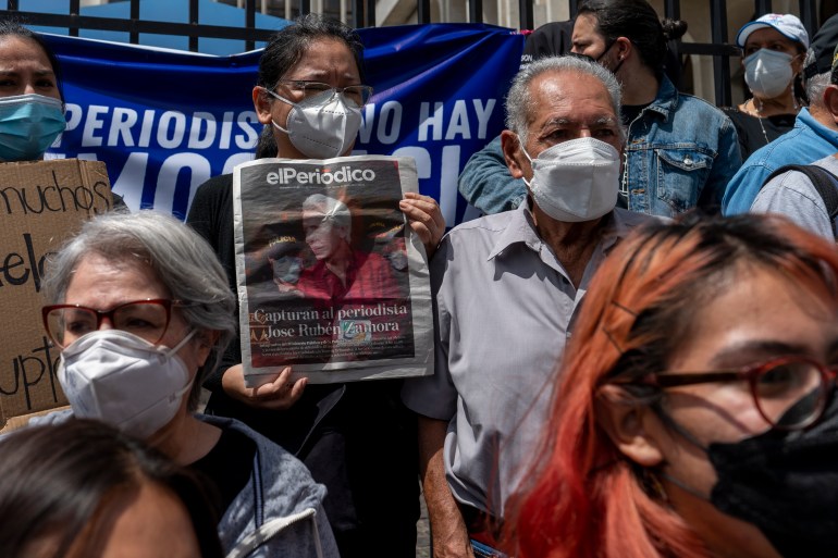 Para jurnalis berkumpul di luar pengadilan untuk memprotes penahanan jurnalis pemenang penghargaan Jose Ruben Zamora, yang ditangkap sehari sebelumnya, di Guatemala City, Sabtu 30 Juli.  Sebuah spanduk biru terlihat pada protes mereka, dan salah satunya memegang salinan surat kabar El Periodico.