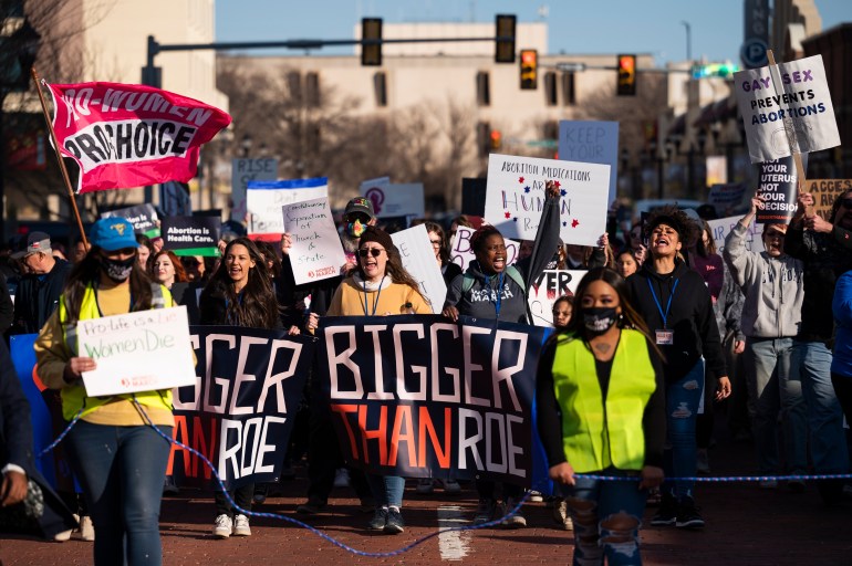 A photo of a group of people protesting and marching holding signs that say a variety of things including "Bigger than Roe", "Pro-choice" and "abortion medications are human rights".