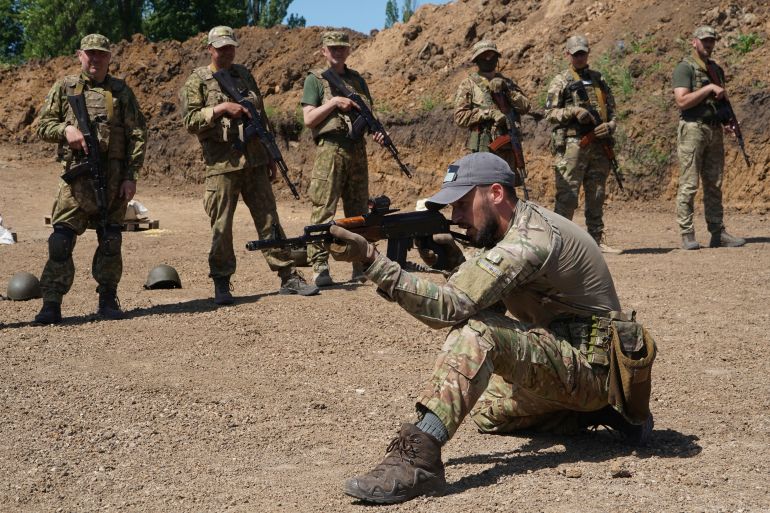 Servicemen of the newly created National Guard unit train in Ukraine's Kharkiv region. A man is one one knee holding up his rifle. Others are behind him.