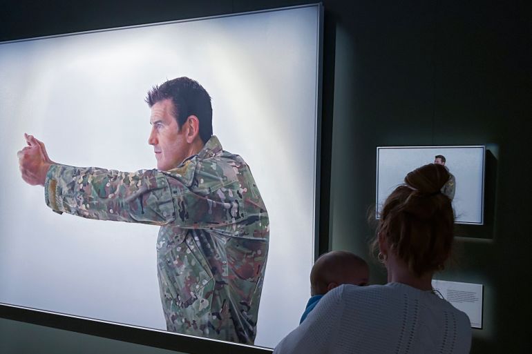 A woman looking at the portrait of Ben Roberts-Smith called Pistol Grip. He is depicted in combat uniform in a fighting stance.