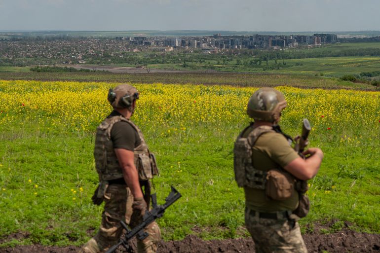 Two Ukrainian soldiers near Bakhmut. The town is far in the background with green fields dotted with yellow flowers in between.