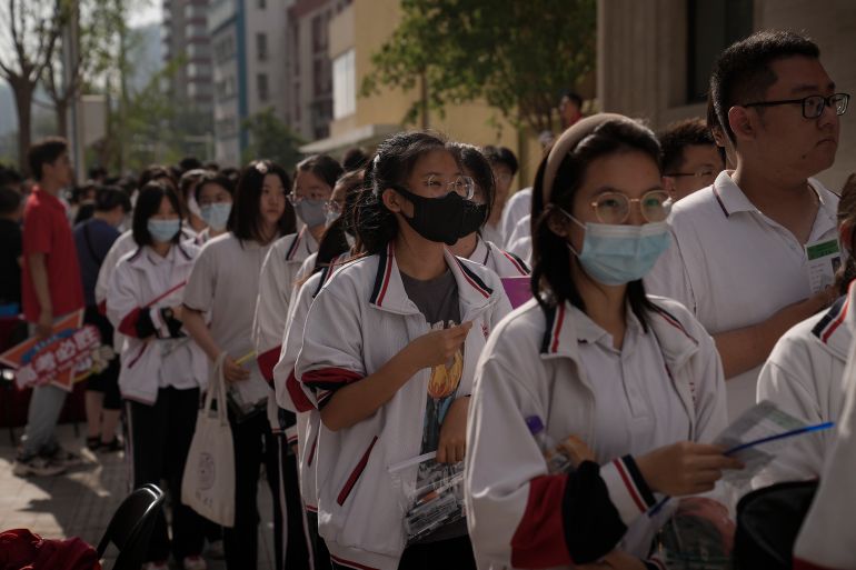 Students head into school on the first day of China's gaokao exams. They are wearing white uniforms and face masks,