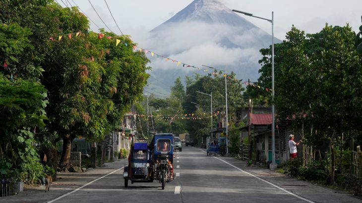 A woman drives a tricycle as Mayon volcano is seen from Legazpi, Albay province, northeastern Philippines, Tuesday, June 13, 2023