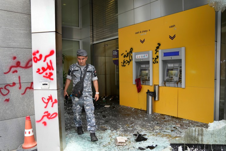 A policeman walks past Byblos Bank vandalized by angry protesters 