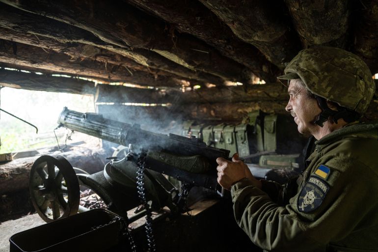 A Ukrainian soldier shooting a Maxim gun towards Russian positions on the front line. He is in a concealed bunker. There is smoke rising from the gun.