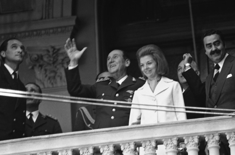 A black-and-white photo of a couple on the balcony of a government building, waving to crowds unseen.