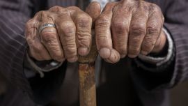 A pair of hands that belong to an elderly man rest on a cane.