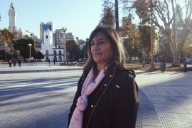 A woman in a pink scarf and dark jacket stands in a Buenos Aires plaza.
