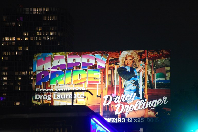 A billboard reads: "Happy Pride from your new drag laureate, D'Arcy Drollinger"