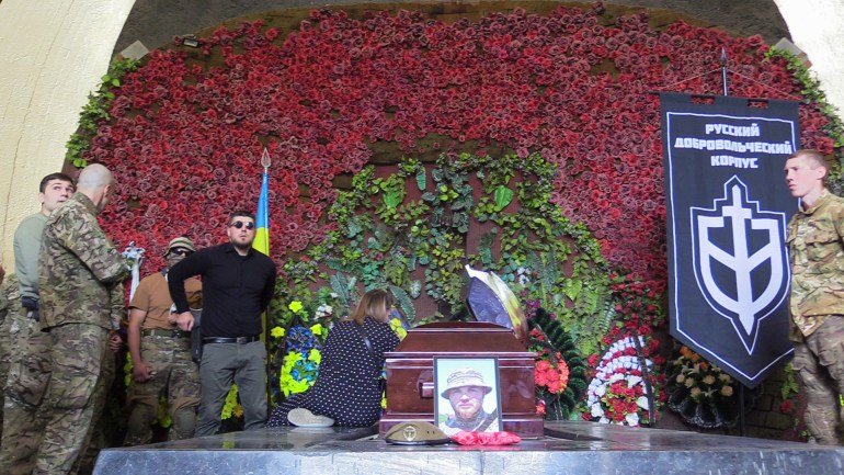 Denis Kapustin, clad in black, stands next to the coffin of Daniil Maznik and the banner of the Russian Volunteer Corps-1686824350