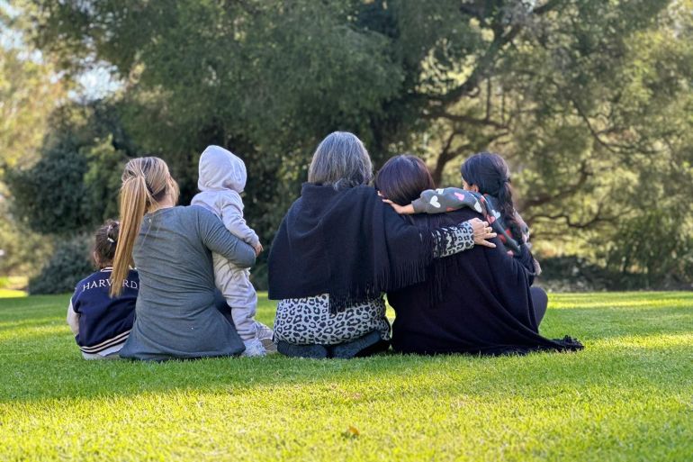 A family of Iranian refugees sitting outside together in a park. One young woman is holding her toddler