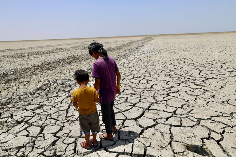 Two young boys from the village, 13-year-old Rusool and 6-year-old Waad, explore the cracked ground where the water used to sit.