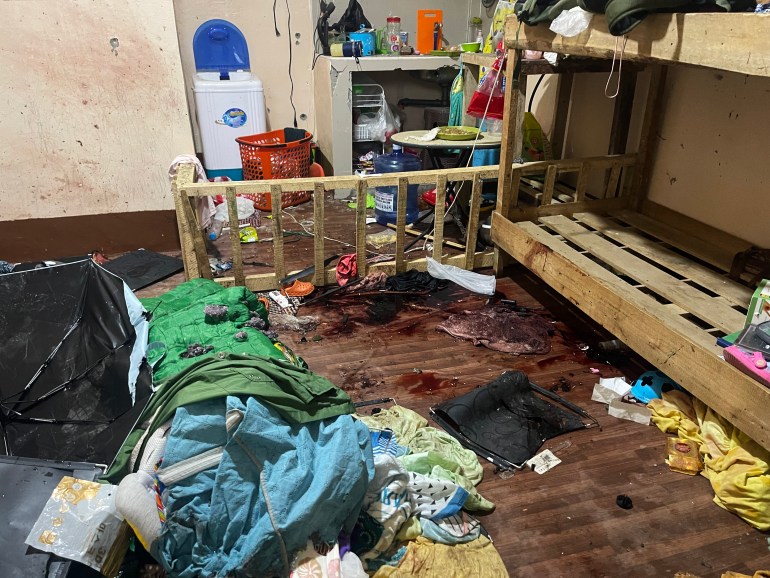 Blankets, sleeping bags strewn about after a raid on the hideout of Abu Zacharia. There are blood stains on the wooden cot. There is a cooking area and water cooler behind.