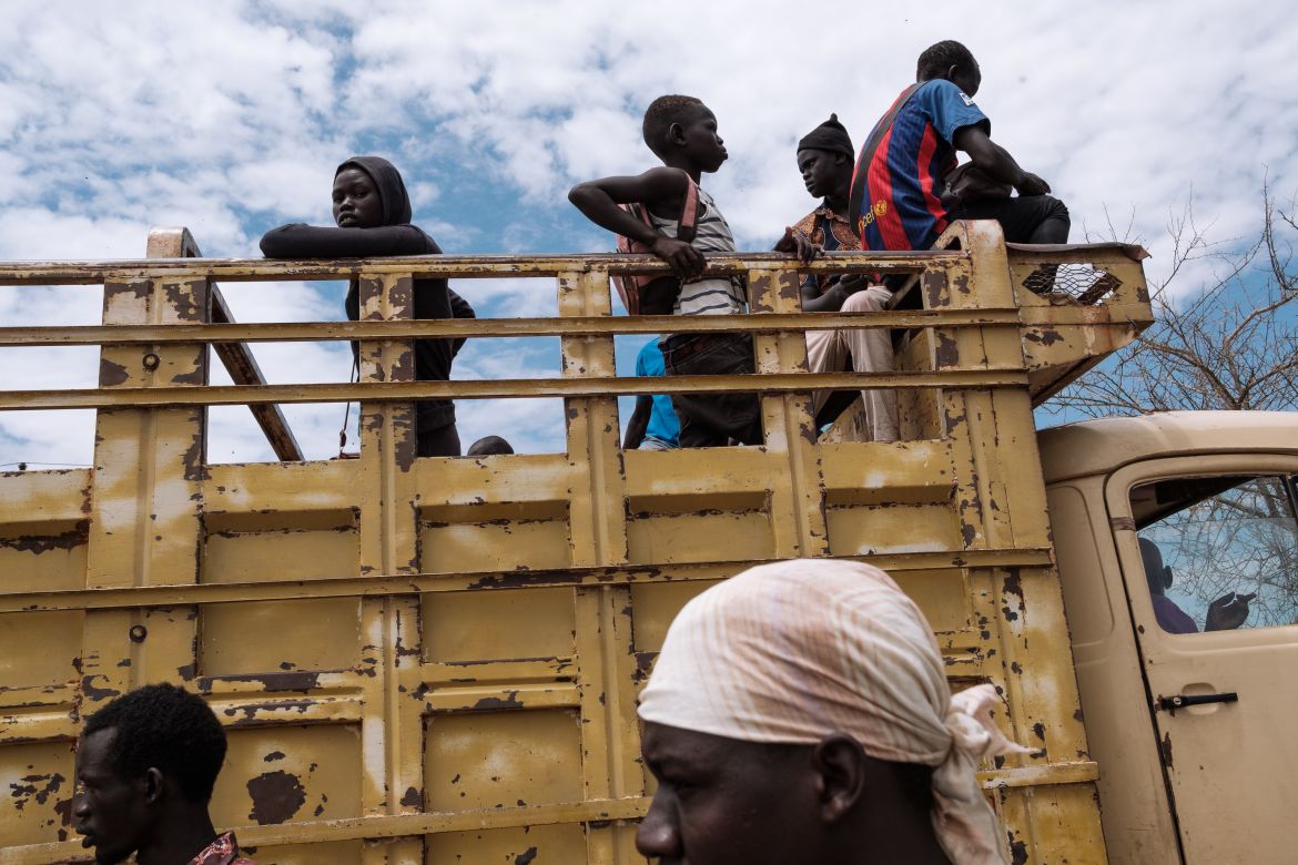 Returnees climb onto the back of a large truck at the Renk