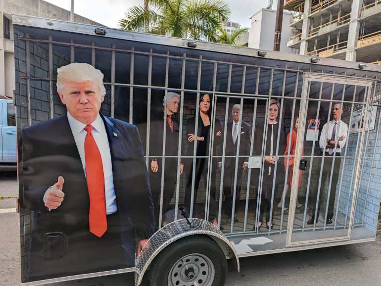 Sebuah trailer di luar gedung pengadilan Miami di mana mantan Presiden AS Donald Trump tampaknya didakwa menunjukkan Trump mengacungkan jempol dan para pemimpin Demokrat di balik jeruji besi.  Dari kiri ke kanan Trump, Bill Clinton, Kamala Harris, Joe Biden, Hilary Clinton, Nancy Pelosi and Barack Obama (Ali Harb/Al Jazeera)