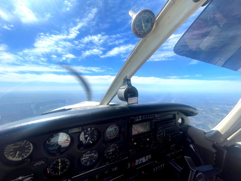 A photo of the pilot's view of the controls and window in a small plane with the ocean below.