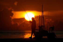 A man fishes with a shimmering sun in the background