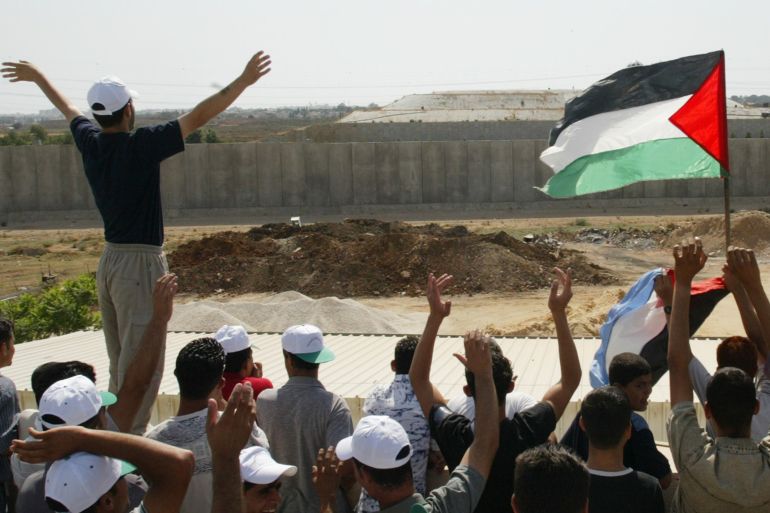 Palestinian demonstrators wave towards Israeli activist on the other side of the Israeli security wall during a rally against the separation barrier, seen in the background, that took place on both sides of the barrier near the West Bank town of Qalqiliya July 16, 2004.