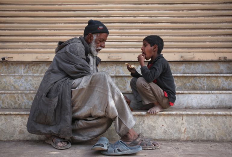 A man and child eat food that they begged for from a nearby food stall, outside a closed shop in Karachi