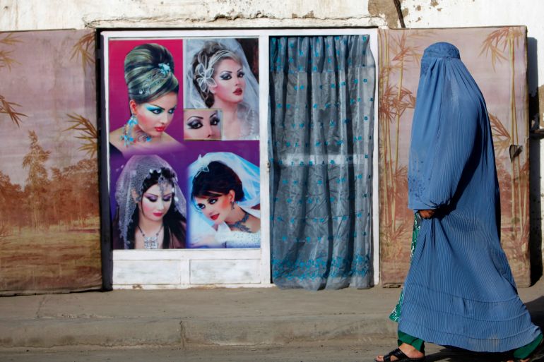 An Afghan woman in a burqa walks past a beauty saloon shop in Kabul