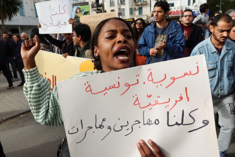 A woman carries a banner, which reads: "Feminist, Tunisian, African. We are all men and women immigrants", during a protest after Tunisian President Kais Saied ordered security forces to stop all illegal migration and expel all undocumented migrants, in Tunis, Tunisia