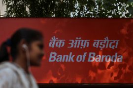 A woman walks past a signboard of Bank of Baroda outside their branch office in New Delhi, India