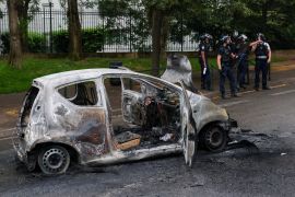 French police officers stand next to a car burnt during a night of clashes between protesters and police