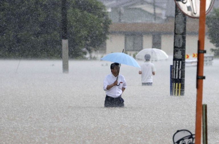 Orang-orang berjalan di jalan yang banjir di tengah hujan lebat di Kurume
