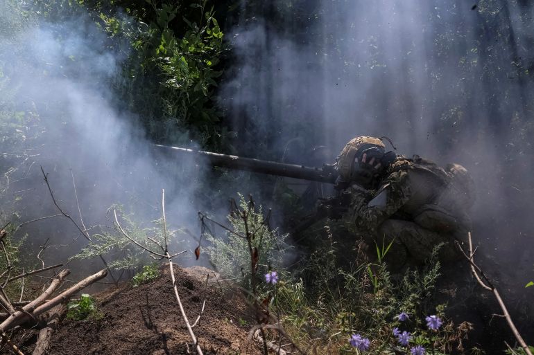 A Ukrainian soldier firing an anti-tank grenade launcher on the front line. He is crouched down, There are bushes around and some smoke.