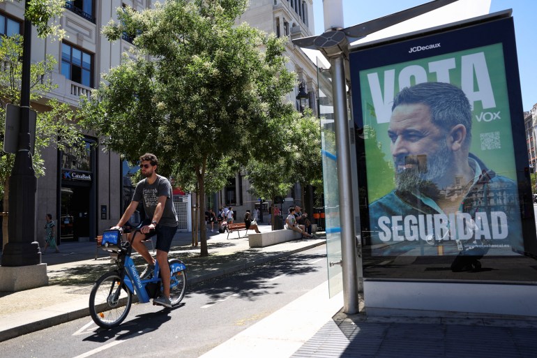 Seseorang mengendarai sepeda di jalur sepeda melewati poster kampanye pemilihan umum