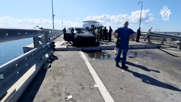 Russian investigators and emergency services' members gather near a destroyed car at the accident scene on the damaged section of a road following an alleged attack on the Crimea Bridge, that connects the Russian mainland with the Crimean peninsula across the Kerch Strait, in this still image taken from video released July 17, 2023. Investigative Committee of Russia/Handout via REUTERS ATTENTION EDITORS - THIS IMAGE WAS PROVIDED BY A THIRD PARTY. NO RESALES. NO ARCHIVES. MANDATORY CREDIT. WATERMARK FROM SOURCE.  