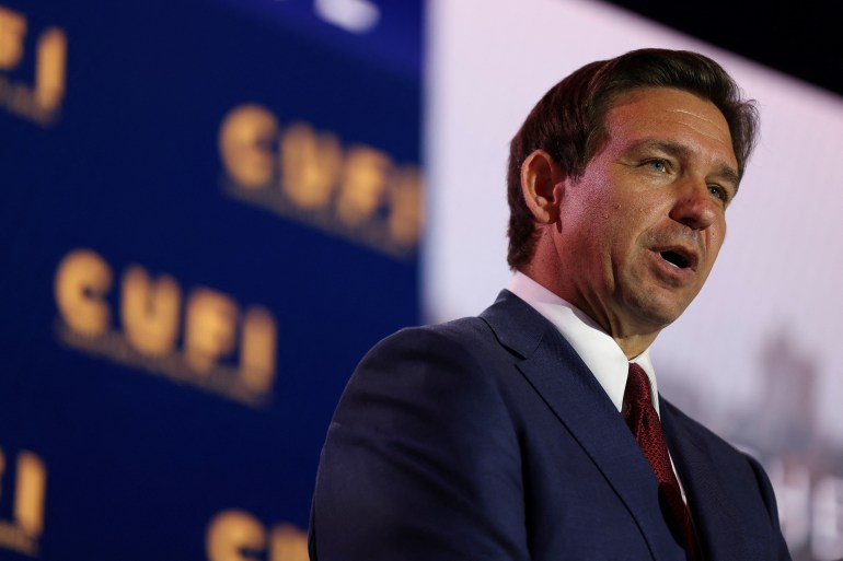 Ron DeSantis stands in a suit and tie front of a banner with the CUFI logo