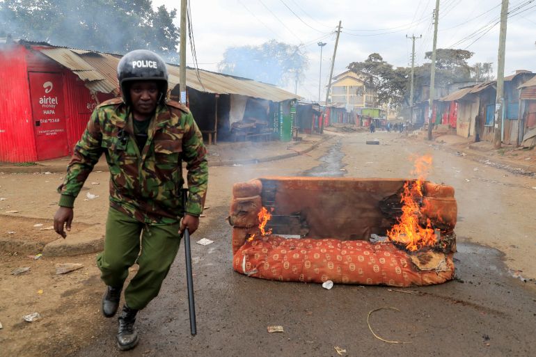 A riot police officer runs next to a burning sofa, as supporters of Kenya's opposition leader Raila Odinga of the Azimio La Umoja coalition participate in an anti-government protest against tax hikes by the government in Nairobi, Kenya