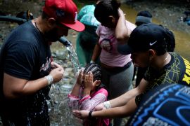 A family of Venezuelan migrants clean themselves with water from a pipe