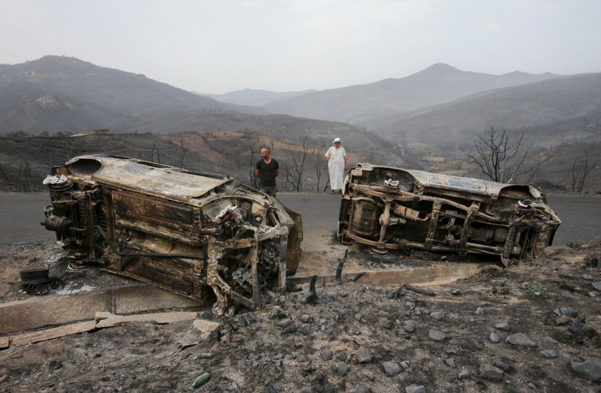 Men stand near burnt vehicles, in the aftermath of a wildfire in Bejaia, Algeria