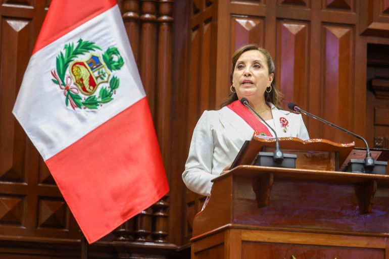 Peru's President Dina Boluarte delivers her address to the nation at the Legislative Palace, in Lima, Peru, July 28, 2023. She stands at a wooden podium, in a wood-panelled room, with the Peruvian flag next to her.