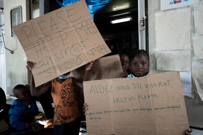 Refugee children hold signs on board the Ocean Viking ship sailing in the Strait of Sicily in the Mediterranean Sea on November 3, 2022, after being rescued by European maritime-humanitarian organisation "SOS Mediterranee".