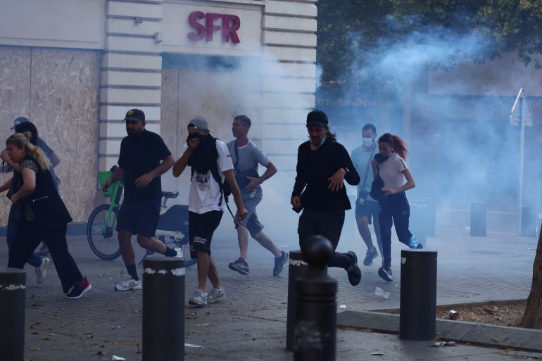 Protesters run from launched tear gas canisters during clashes with police in Marseille, southern France