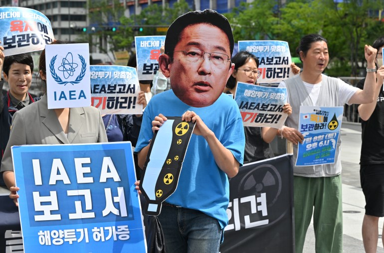 Pengunjuk rasa Korea Selatan mengadakan unjuk rasa menentang rencana pelepasan air Fukushima.  Seseorang memakai topeng Perdana Menteri Jepang Fumio Kishida.  Lainnya memiliki plakat dalam bahasa Korea yang bertuliskan IAEA 