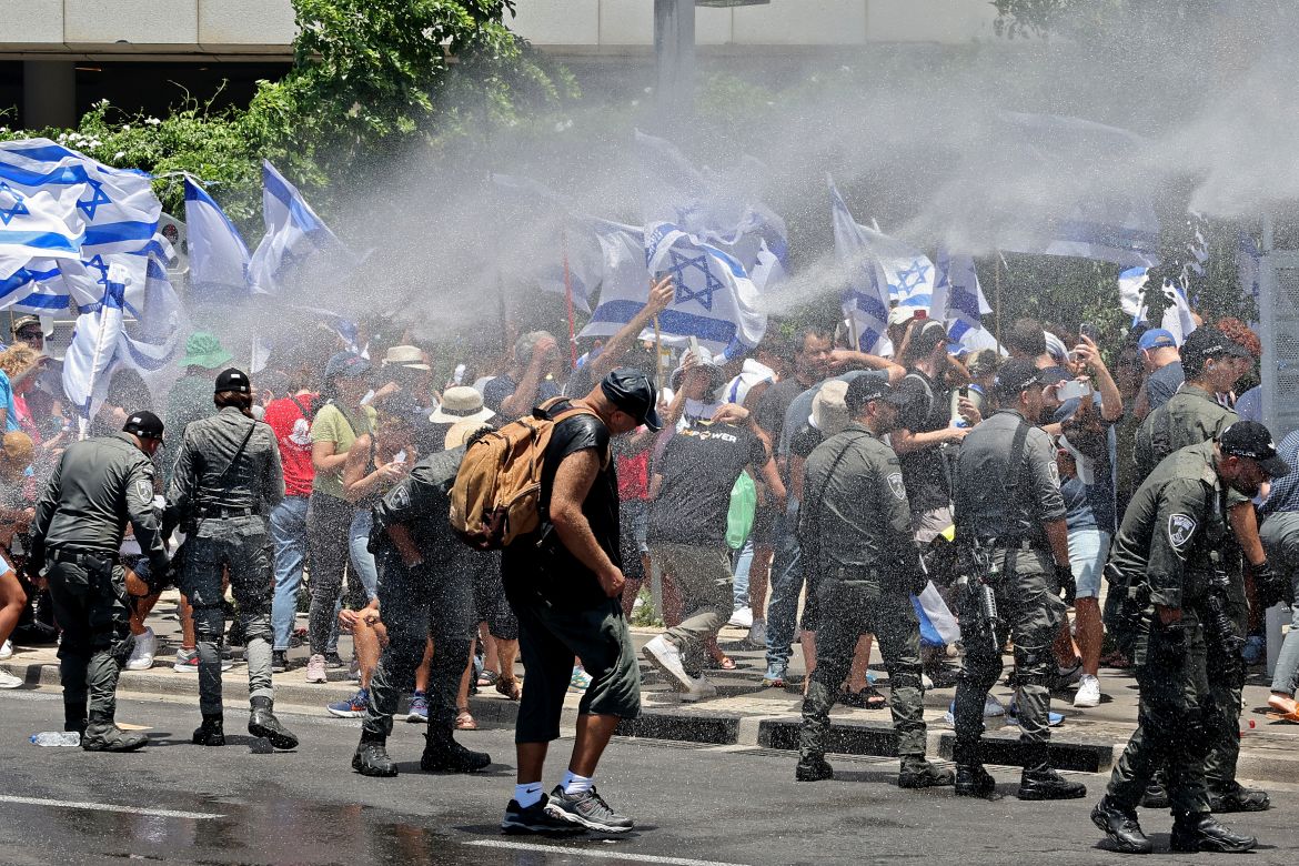 Demonstrators wave flags as they are sprayed with water by Israel's police