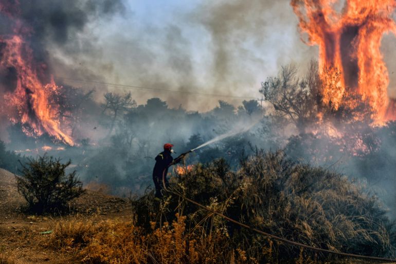 A fireman douses flames on a wildfire at Panorama settlement near Agioi Theodori, some 70 kms west of Athens on July 18, 2023. - Europe braced for new high temperatures on July 18, 2023, under a relentless heatwave and wildfires that have scorched swathes of the Northern Hemisphere, forcing the evacuation of 1,200 children close to a Greek seaside resort. Health authorities have sounded alarms from North America to Europe and Asia, urging people to stay hydrated and shelter from the burning sun, in a stark reminder of the effects of global warming. (Photo by Valerie GACHE / AFP)