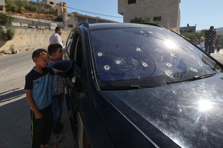 Anak-anak berdiri di samping mobil yang penuh dengan peluru tempat seorang Palestina tewas
